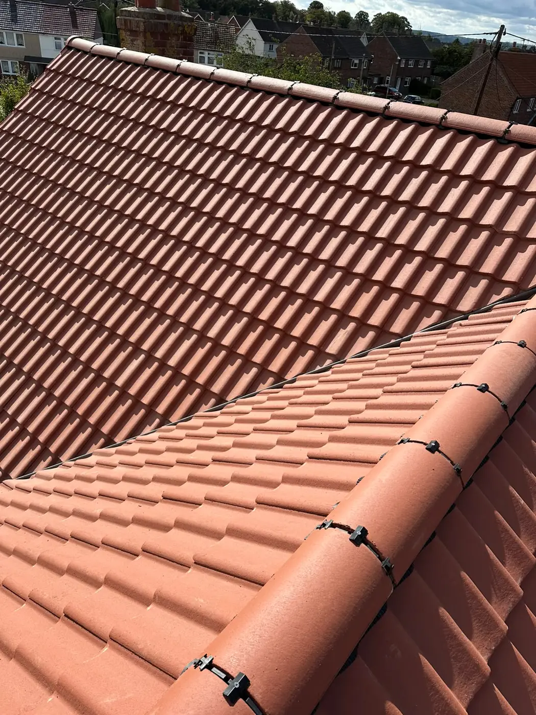 Two slopes of new terracotta pantiles meeting with dry fixed ridge tiles in Holt