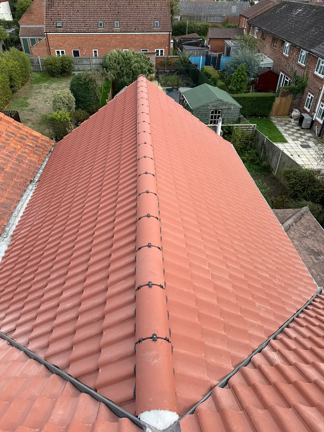 Hipped terracotta pantile roof from above with central ridge and neighbouring gardens in Holt