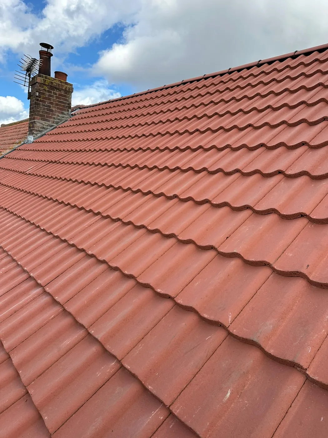 Red pantile roof sweeping up to a chimney stack with television aerial in Holt
