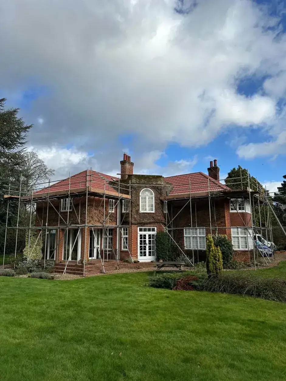Large period house under scaffold with half the roof re-covered in new red tiles