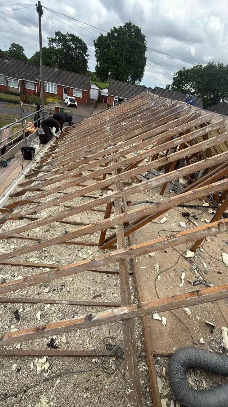 Roof stripped to bare rafters with spray foam debris across the ceiling below
