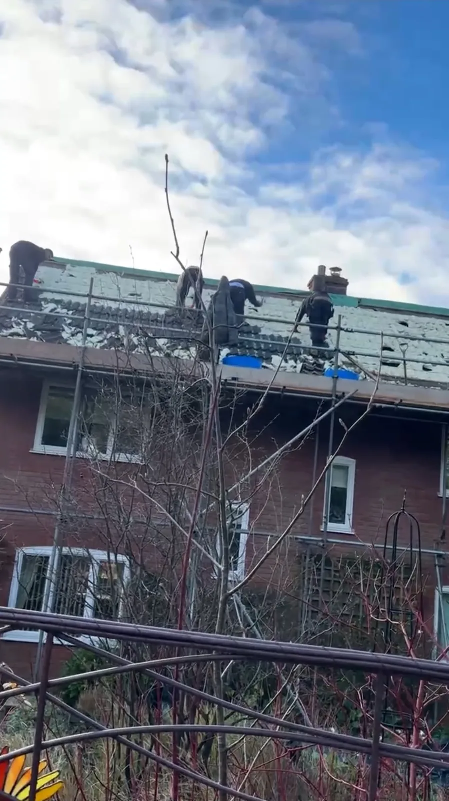 Roofers on a scaffold stripping the covering from a roof